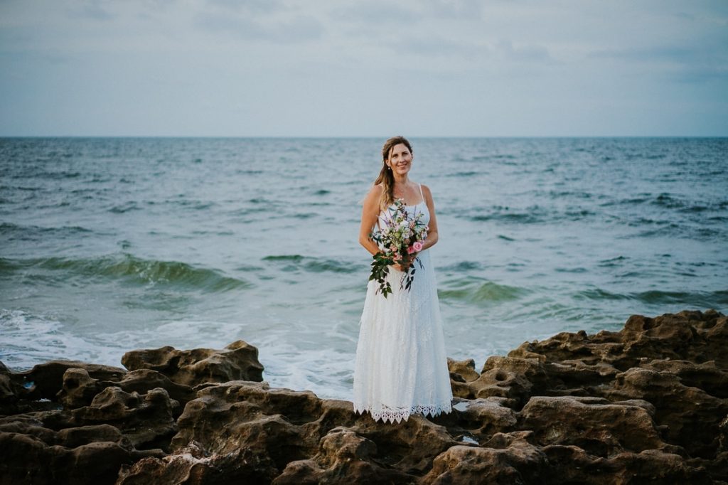 Coral Cove beach elopement bride in white lace beach wedding dress holding bouquet