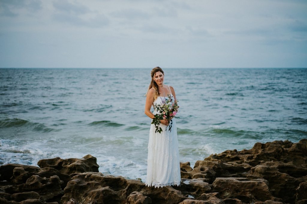 Coral Cove beach elopement bride in white lace beach wedding dress holding bouquet looking down