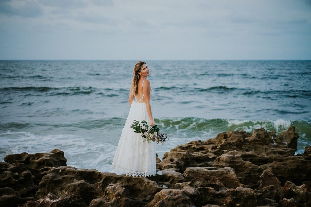 Coral Cove beach elopement bride in white lace beach wedding dress holding bouquet looking over shoulder