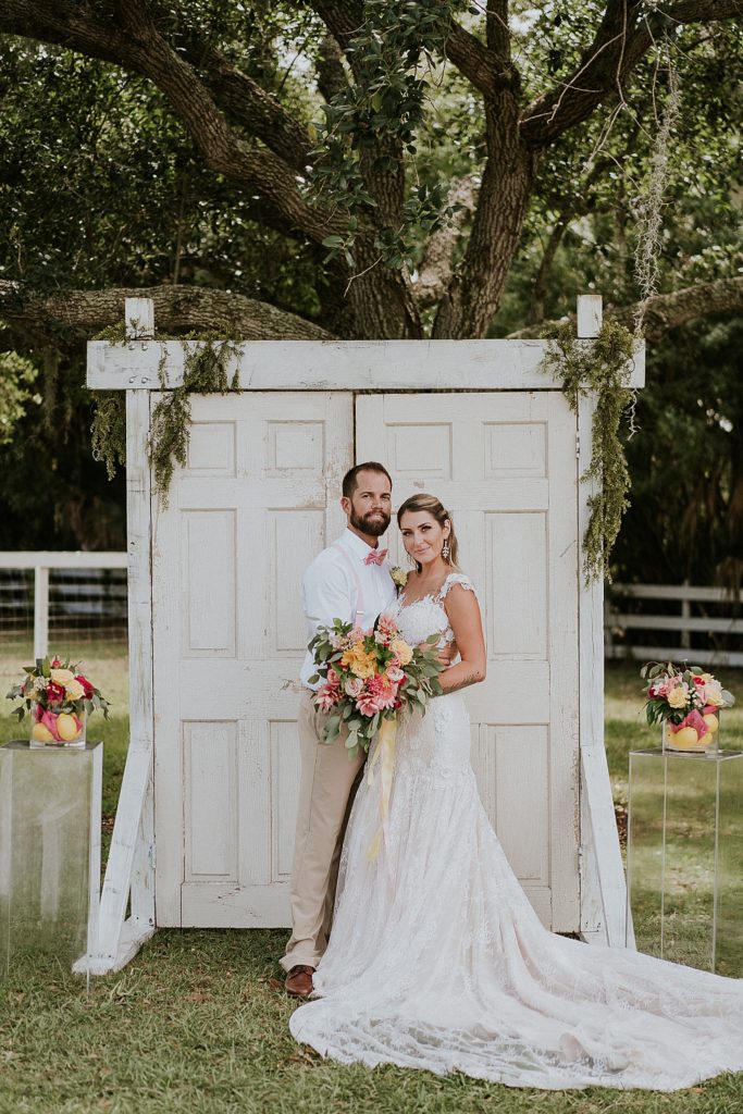 Bride and Groom posing in front of ceremony wedding door under oak tree at Pink Lemonade photoshoot Twisted Oak Farm Vero Beach FL barn wedding