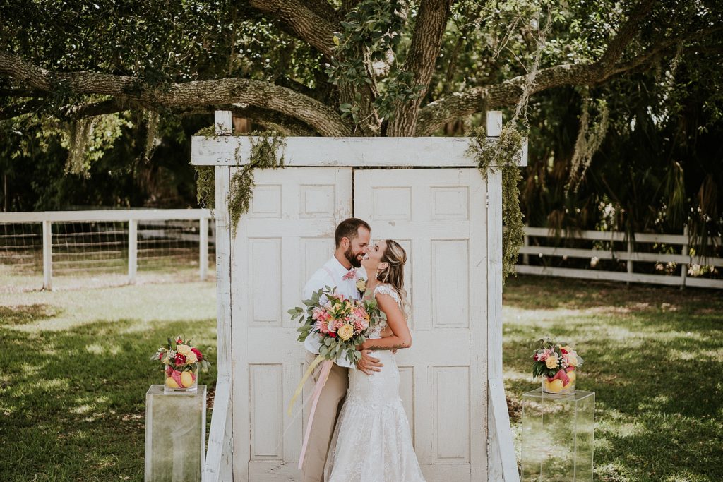 Bride and Groom laughing in front of ceremony wedding door under oak tree at Pink Lemonade photoshoot Twisted Oak Farm Vero Beach FL barn wedding