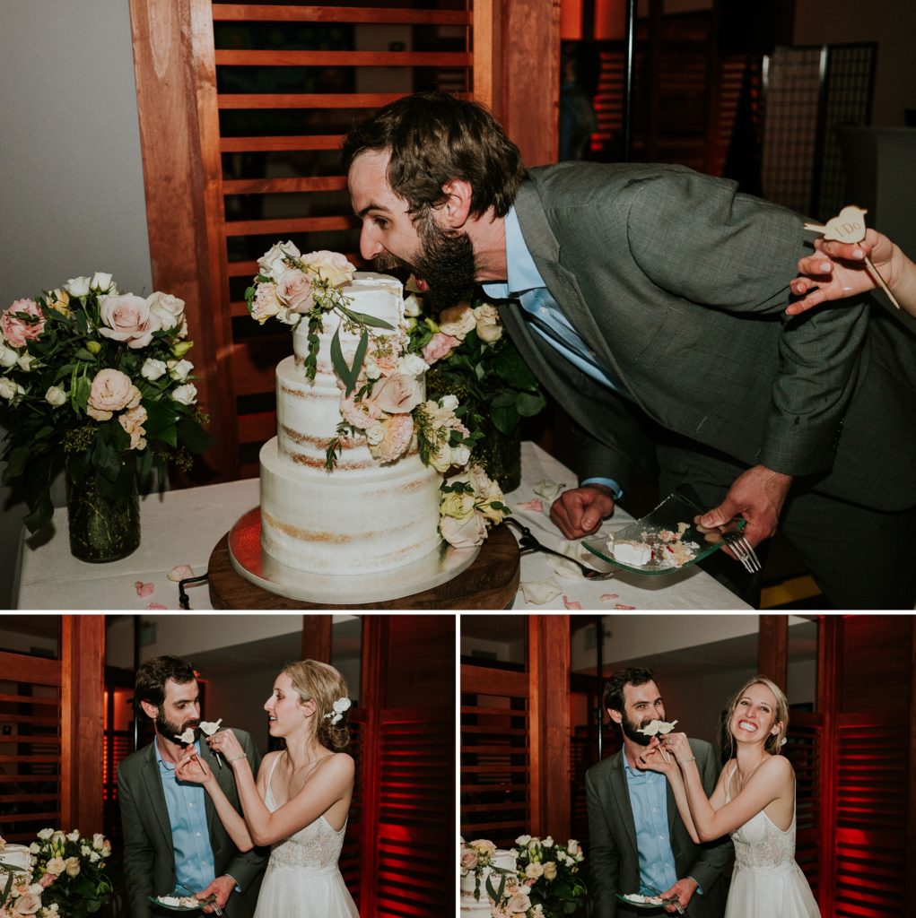 Groom opens his mouth and pretends to dive into wedding cake and eat it and bride holds up cake-toppers as a mustache