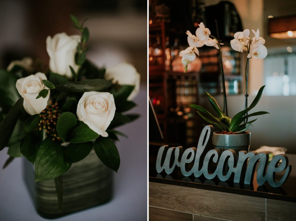 White rose table centerpiece next to white orchids above a grey welcome sign on a table