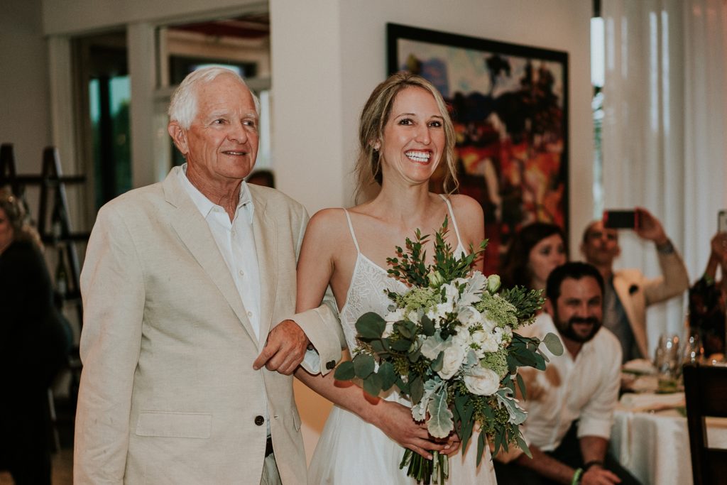 Father of the bride walks bride down the aisle during indoor ceremony