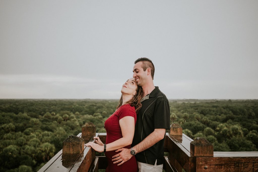 Woman looks up at man with treetops below them while on top of Myakka Canopy Walkway before Sarasota wedding