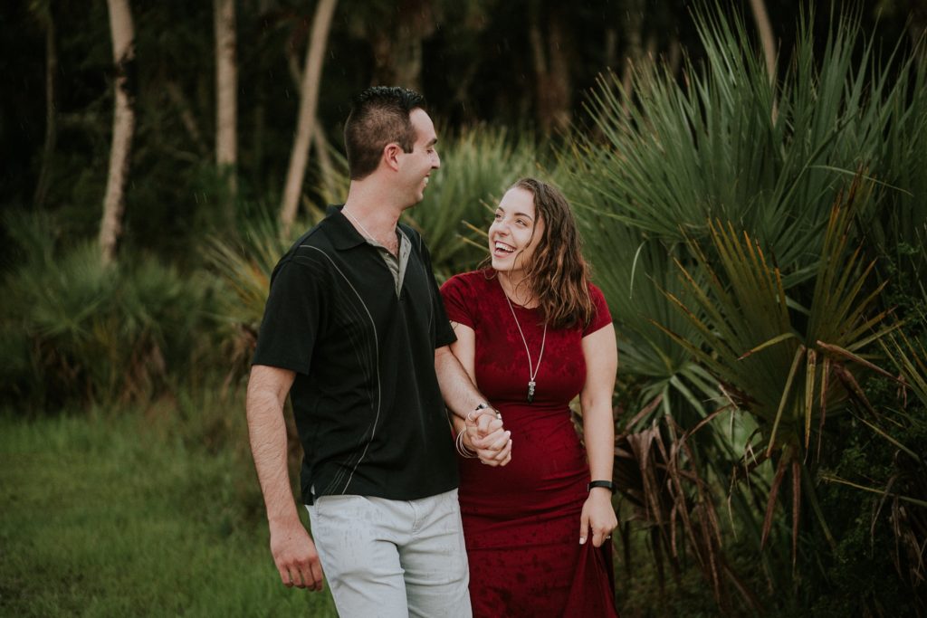 Woman in red dress looks at fiancé lovingly and laughs during engagement session at Myakka river state park before Sarasota wedding
