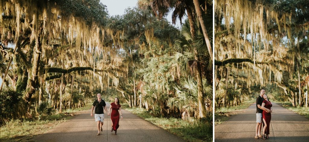 Engaged couple running on a road surrounded by trees and Spanish moss at golden hour
