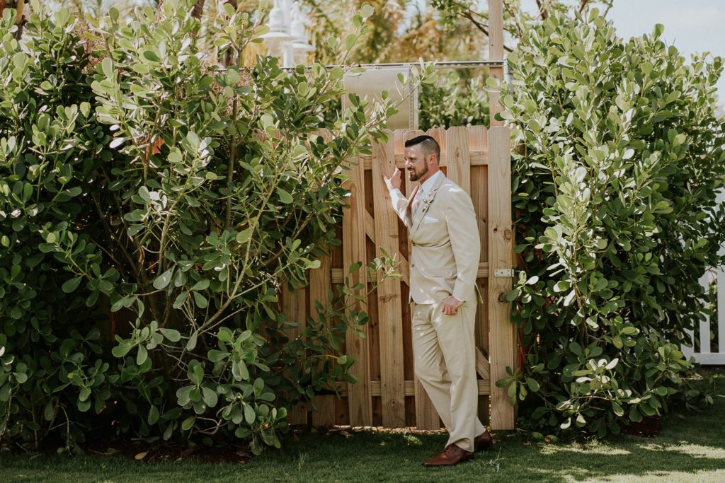 Groom leans on fence wearing khaki suit for summer wedding