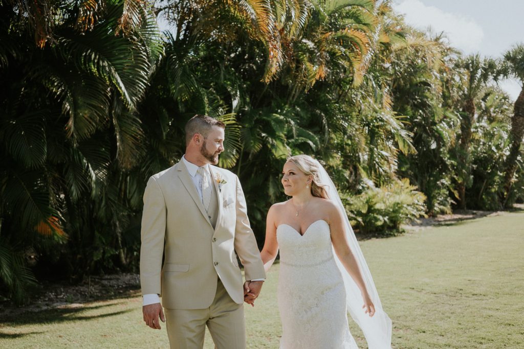 Bride and groom walking, holding hands, looking at each other with palm trees behind