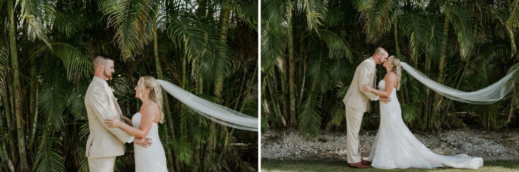 Wedding couple kiss with long cathedral veil flowing behind bride in front of bamboo and green palm fronds at Sailfish Marina on Singer Island
