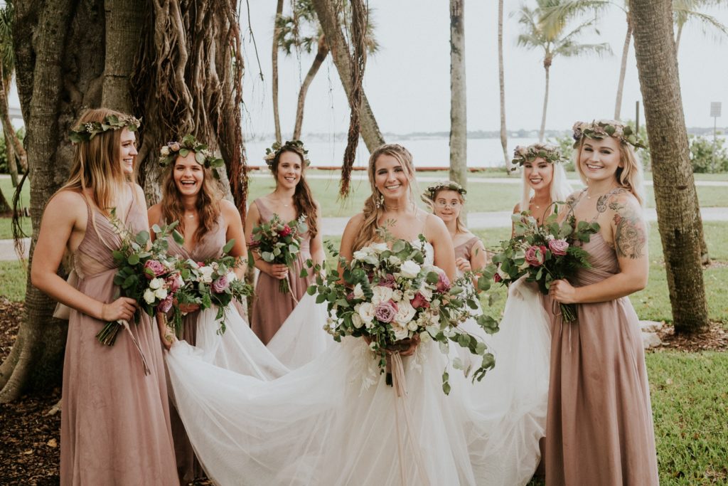 Downtown Stuart FL wedding bridesmaids hold bride's wedding dress under banyan tree in Flagler Park