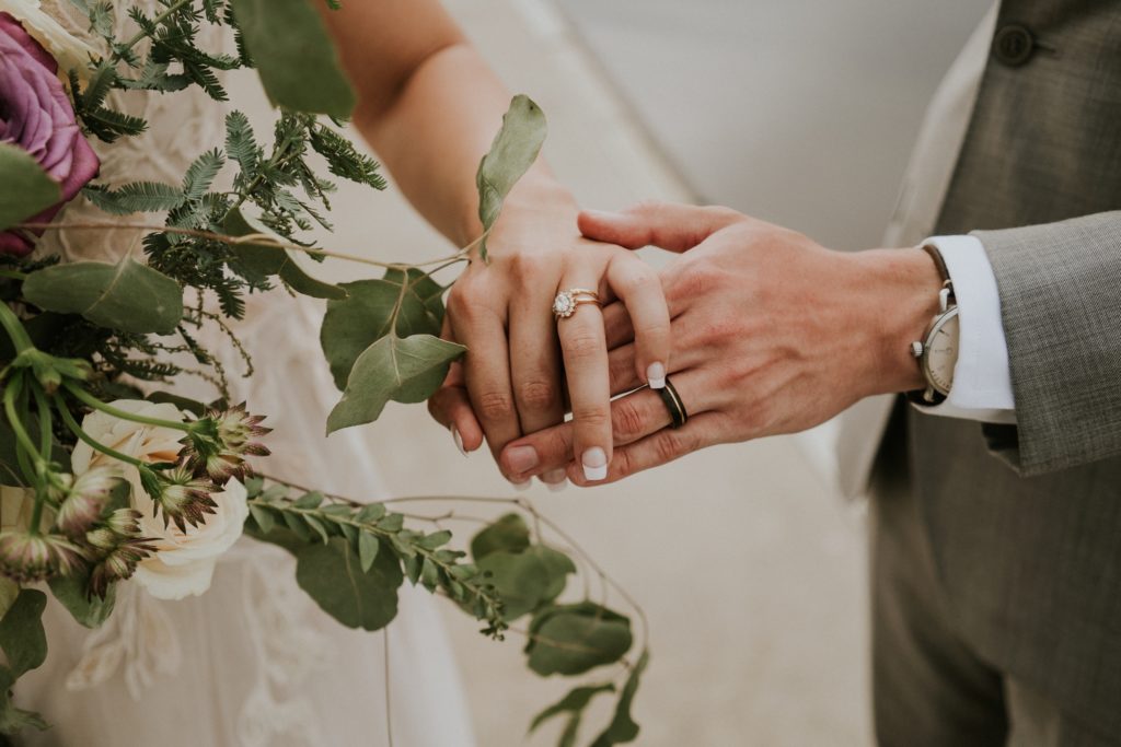 Close up of hands of bride and groom wearing wedding rings by Olive Avenue Jewelry