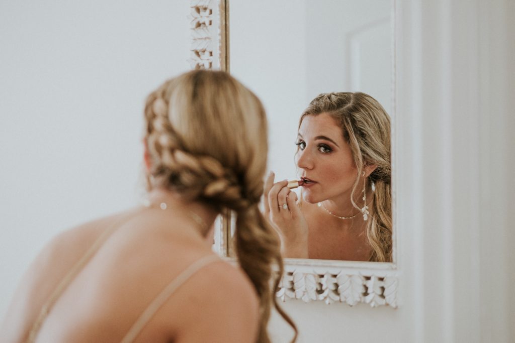 Close up of bride applying lipstick in the mirror with view of her hair in a braided ponytail