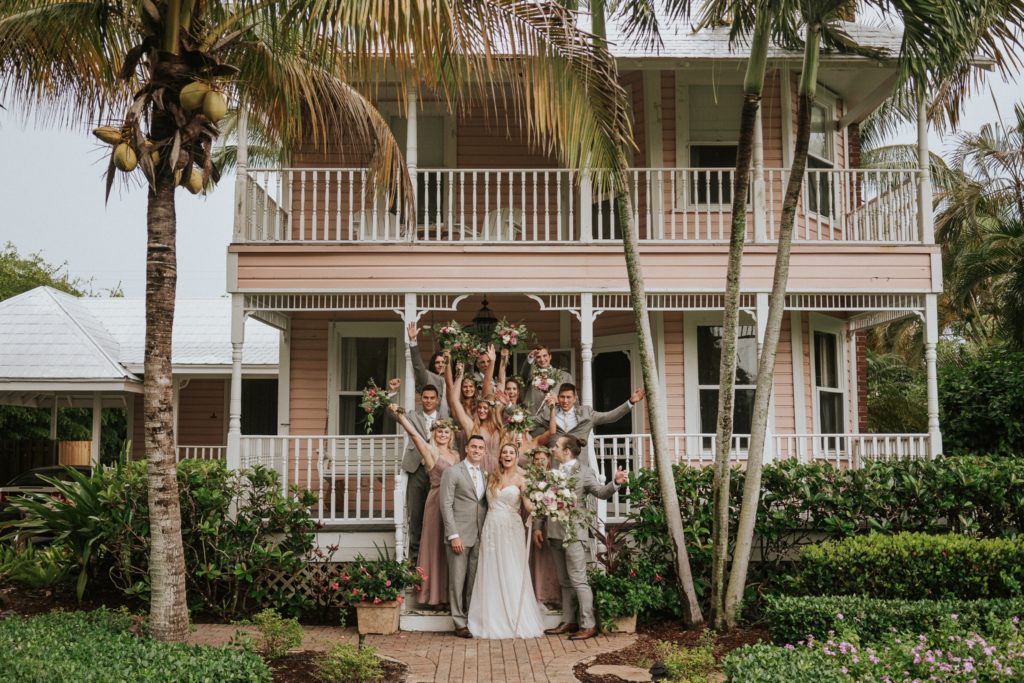 Wedding party cheers with bouquets in the air in front of Downtown Stuart historic pink home