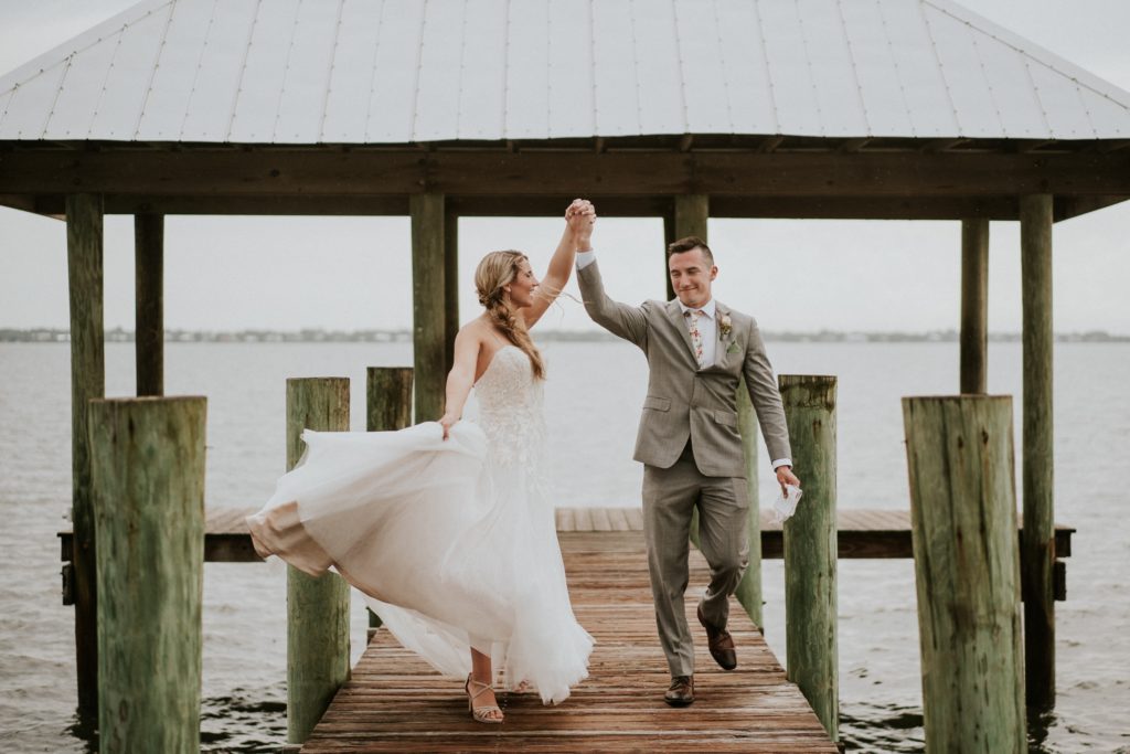 Florida elopement couple joyfully hold hands in the air and walk down boardwalk at House of Refuge dock