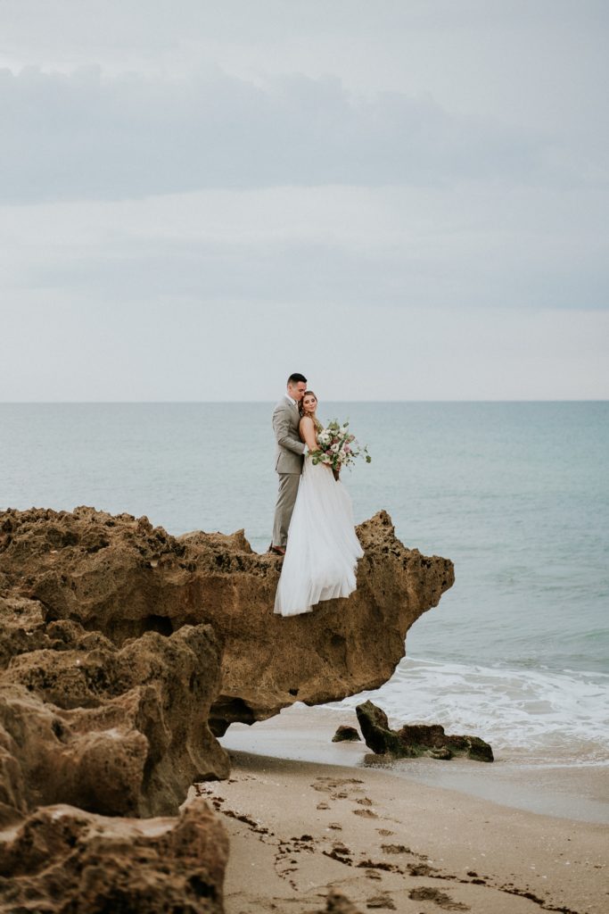 Wedding couple stands on limestone rock above ocean for House of Refuge elopement