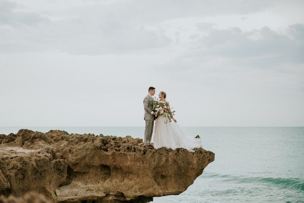 Bride and groom standing on limestone rock for House of Refuge elopement with ocean behind them