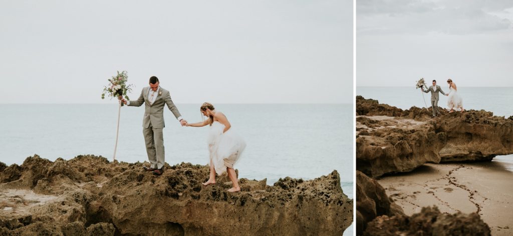 Groom helps bride climb limestone rock at House of Refuge elopement with footprints in the sand below them