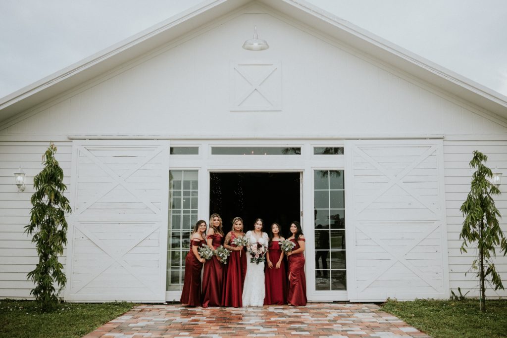 Bride with bridesmaids in red dresses at Ever After Farms Ranch Wedding Barn venue in Indiantown FL