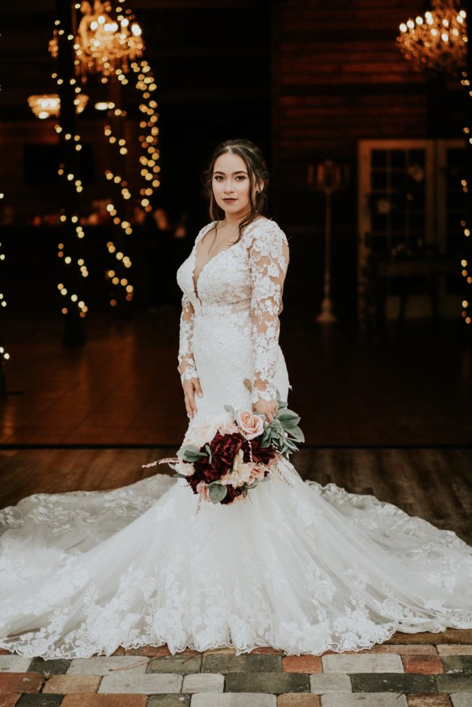 Bride wears white lace floral Martina Liana wedding gown from Boca Raton Bridal with fairy lights behind her