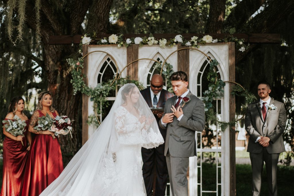Bride claps and groom points to wedding ring during FL barn venue wedding ceremony