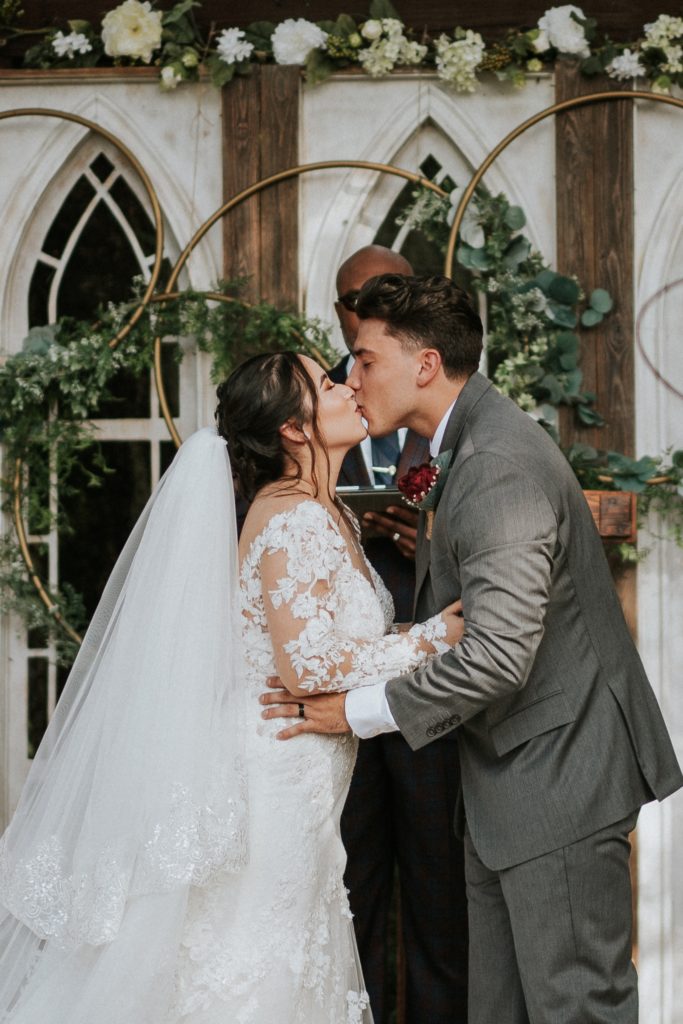 Bride and groom share first kiss in front of white window ceremony backdrop