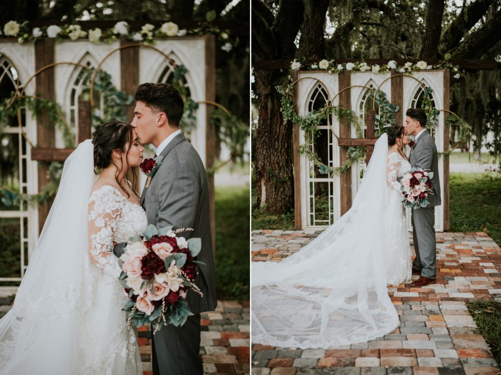 Groom kisses bride's forehead in front of white gothic window wedding arbor ceremony backdrop at Ever After Farms Ranch venue in FL