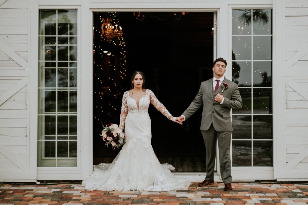 Bride and Groom hold hands in front of white french doors in style of Wes Anderson