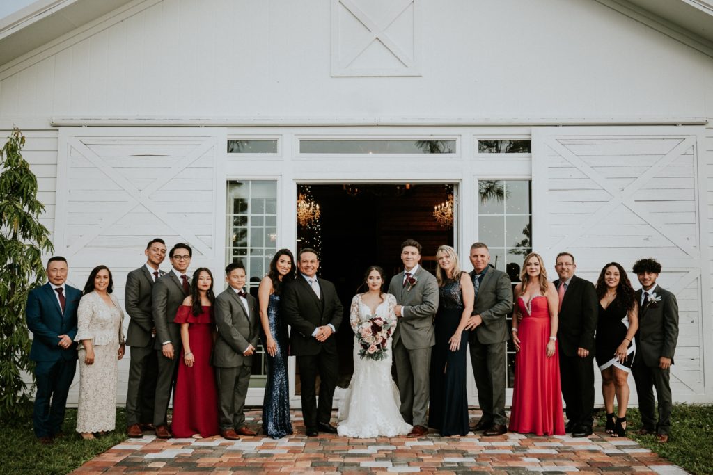 Family of bride and groom stand in front of white barn Fl wedding venue