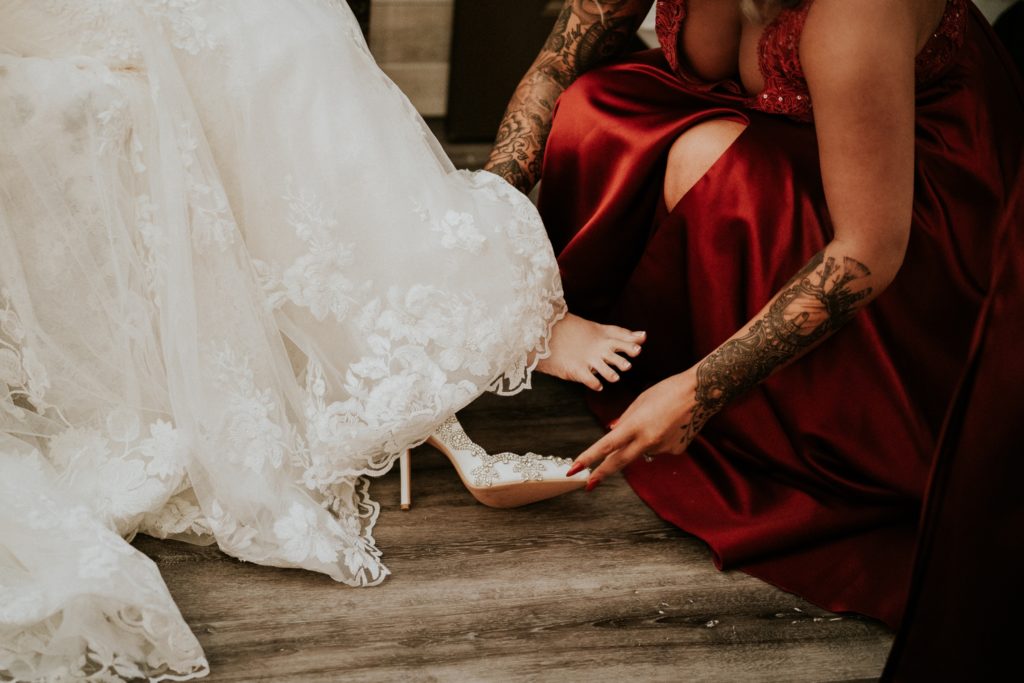 Close up of bridesmaid in red dress putting rhinestone heels on the bride's feet