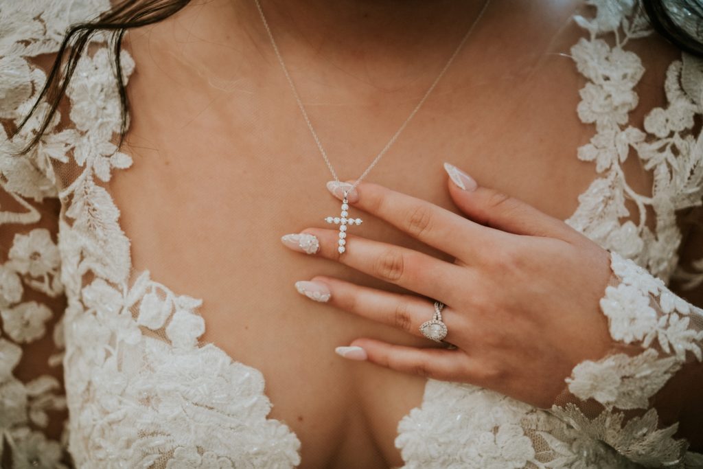 Close up of bride's hand touching her diamond cross pendant necklace