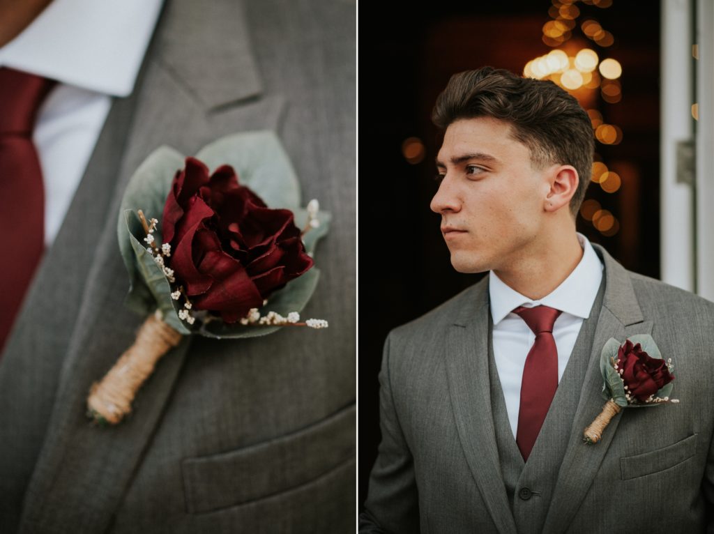 Groom looks away from camera wearing grey suit and red tie with close up of his red rose boutonniere