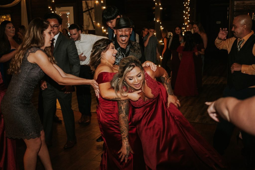Bridesmaids wearing red dresses fall into each other on dancefloor at reception