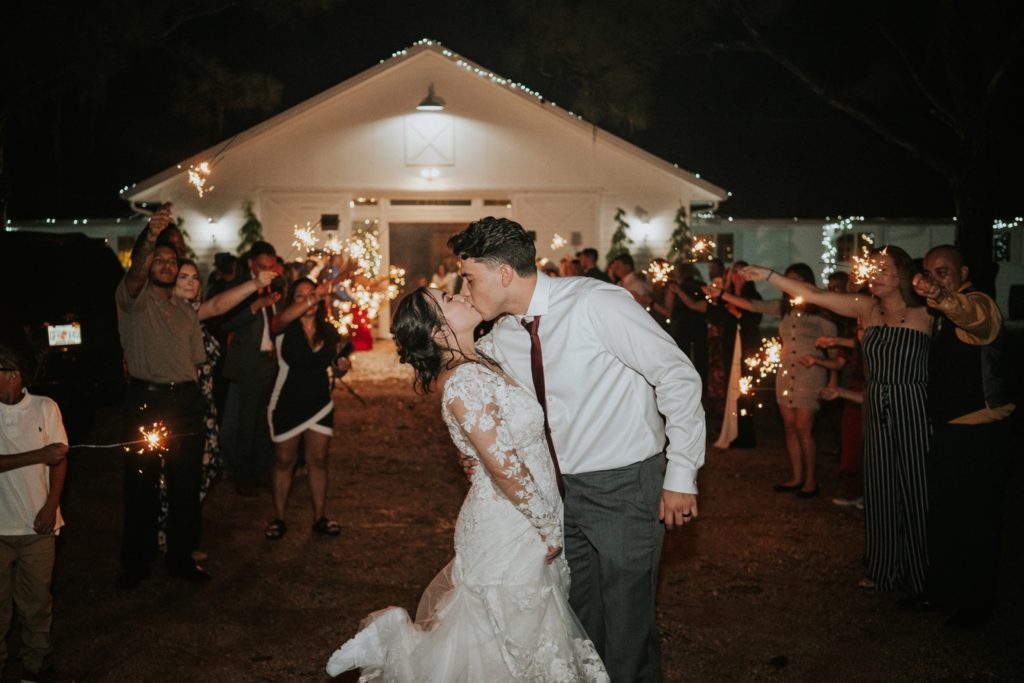 Bride and groom kiss outside of Ever After Farms Ranch Wedding Barn at night for sparkler exit