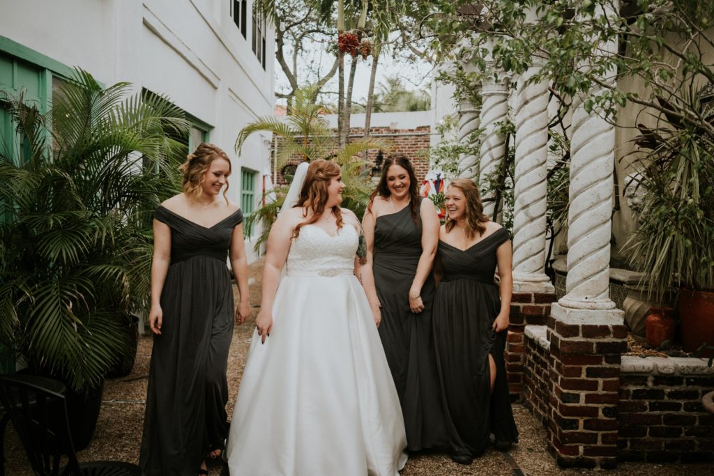 The bride and her sisters wearing green bridesmaid dresses hold hands walking through the Historic Maxwell Room courtyard