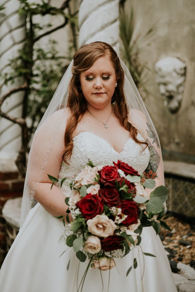Redheaded Bride Allisha looks down at red and pink rose wedding bouquet