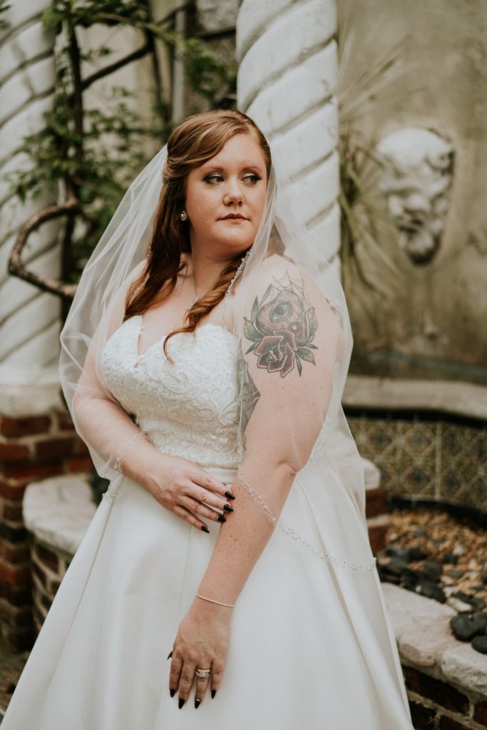 Bride in white wedding dress looks over shoulder with planchette tattoo showing through veil