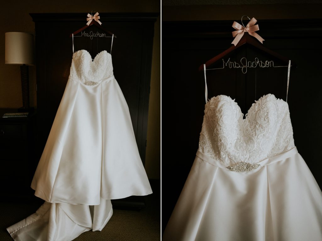 White satin strapless wedding dress with rhinestone belt hanging on wood hanger with pink bow