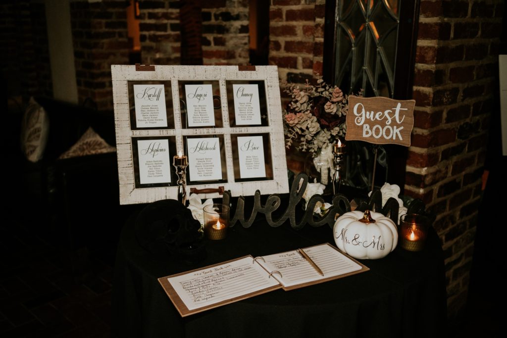 Spooky wedding reception decor with black skull and white pumpkin next to guest book and seating chart