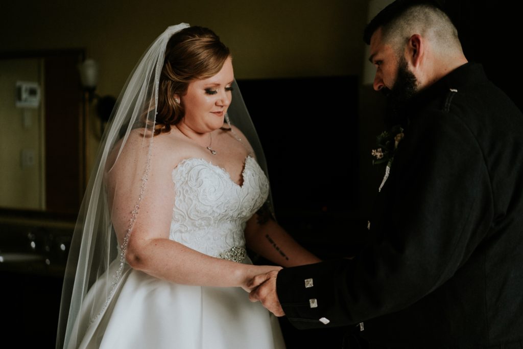 Bride and groom hold hands in dark hotel room after first look
