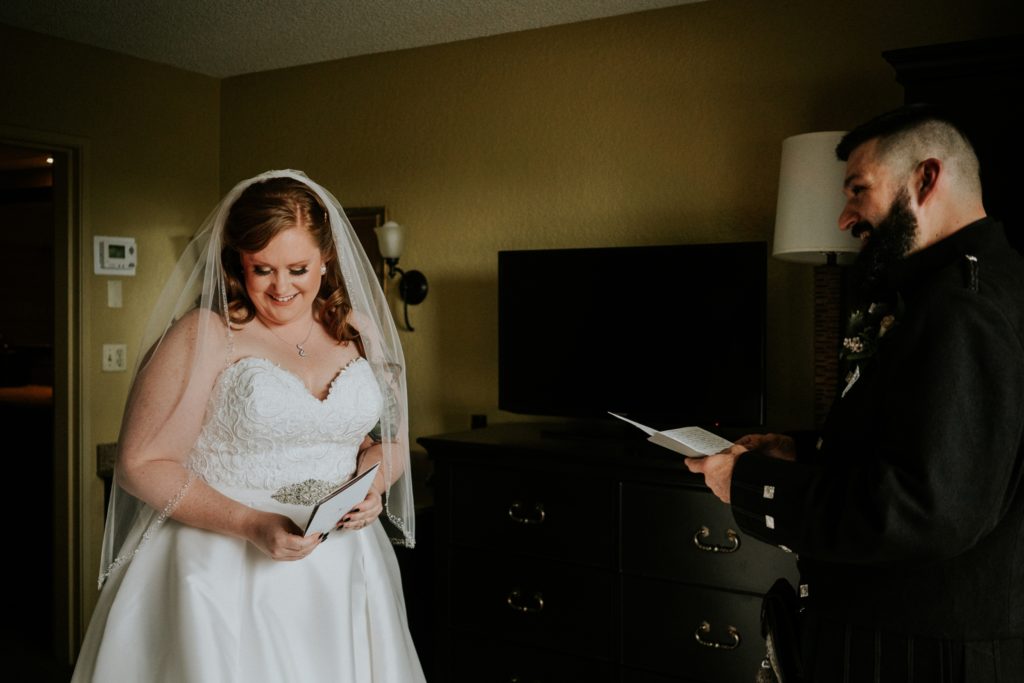 Bride smiles and looks away from groom after exchanging and reading letters in hotel room