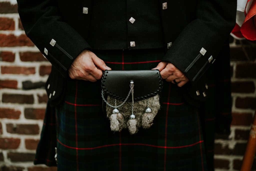 Groom holds animal fur pouch belted to his traditional Scottish wedding kilt attire