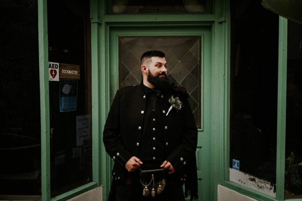 Groom Stan wearing traditional Scottish wedding attire and kilt in front of bright green door