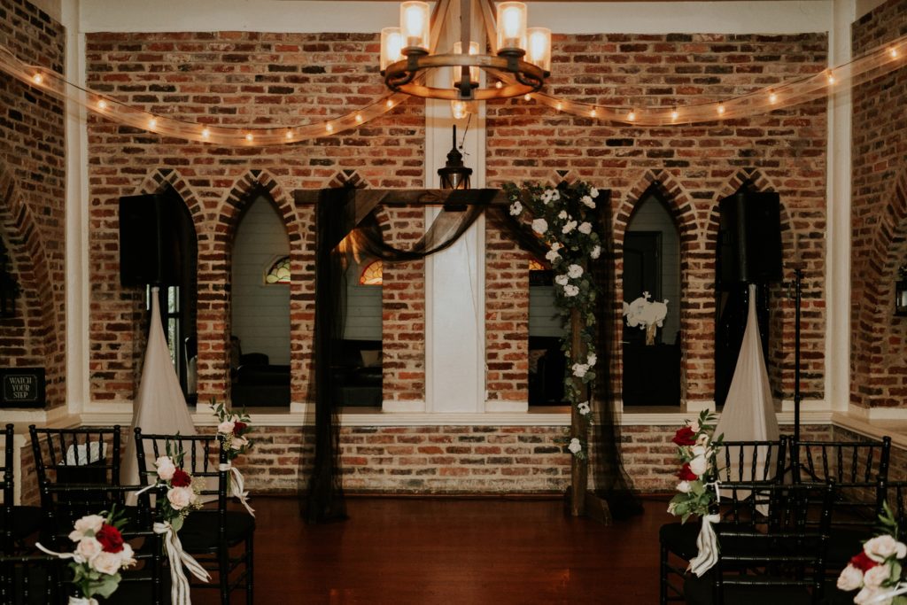 Indoor ceremony setup with wood arch and black chiffon drapery and white flowers in brick Historic Maxwell room
