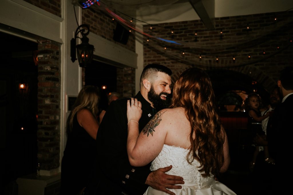 Redheaded bride leans into laughing groom while dancing at reception