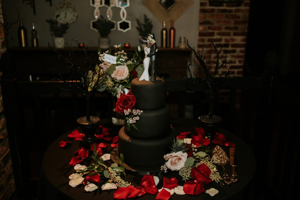 Black fondant goth wedding cake with Bride of Frankenstein and Frankenstein's Monster cake topper surrounded by red rose petals