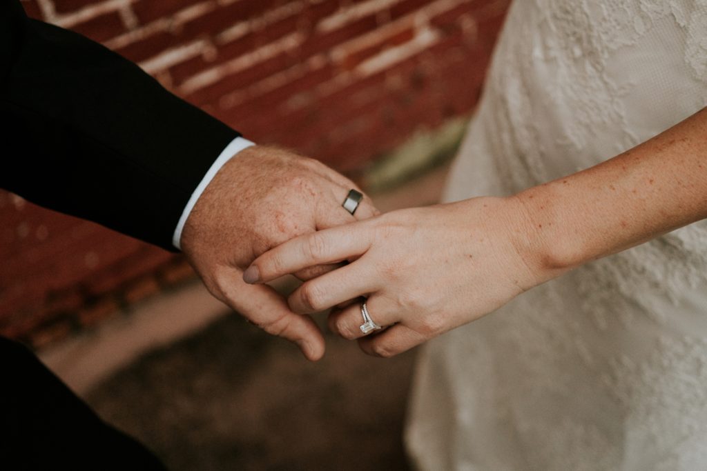 Bride and groom hold hands wearing wedding rings