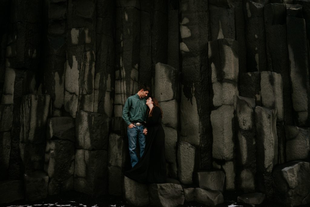 Iceland elopement couple lean on each other on basalt columns at Reynisfjara Black Sand Beach