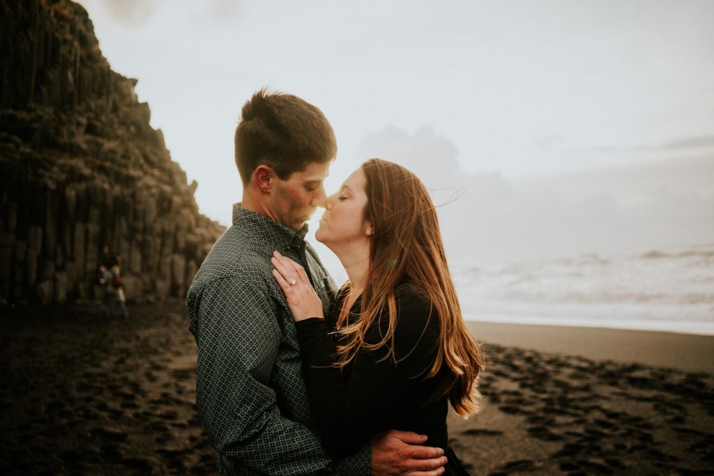 Couple Eskimo kiss noses with sunrise behind them on Black Sand Beach