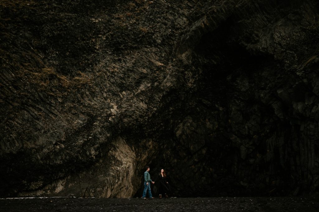Iceland elopement couple walk in front of cave at Reynisfjara Black Sand Beach Vík